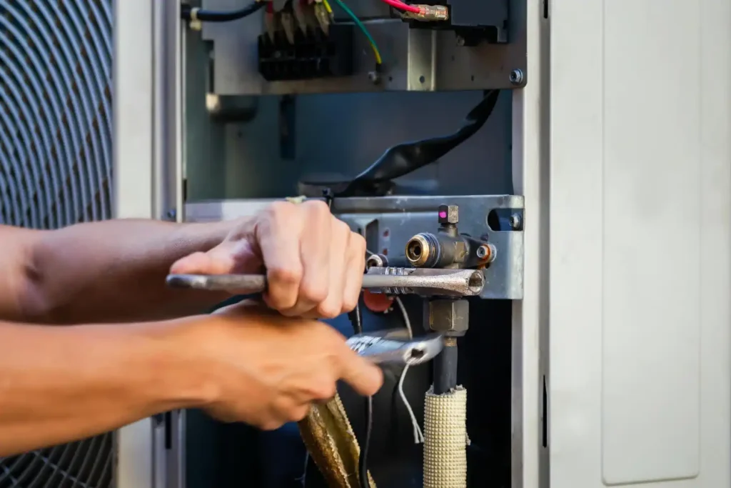 A technician uses tools to repair a Rheem HVAC system, adjusting copper fittings and components inside an open unit.